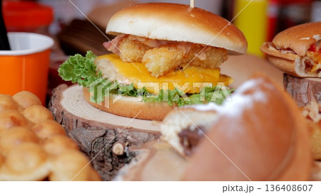 Gourmet sandwich with crispy toppings, Sunny festival stand serving elegant handcrafted burgers, Lively outdoor market offering gourmet burgers with melted cheese and crunchy vegetables on wooden Gourmet sandwich with crispy toppings, Sunny festival stand serving elegant handcrafted burgers, Lively outdoor market offering gourmet burgers with melted cheese and crunchy vegetables on wooden 136408607