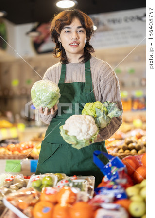 Young female seller offering cauliflower in grocery market Young female seller offering cauliflower in grocery market 136408757