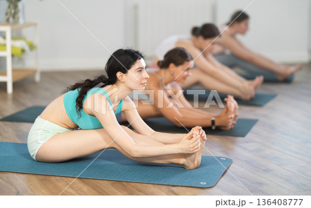 Young girl teaches yoga lesson, shows students technique of performing Janu Shirshasana asana 136408777
