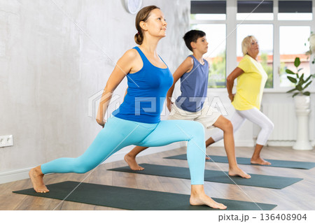 Mother, grandmother and teen son do exercise warrior virabhadrasana pose. 136408904