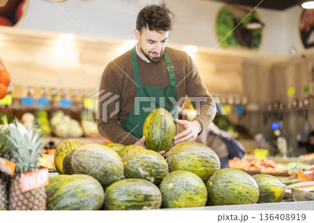 Man seller in grocery vegetable shop arrange melon. 136408919