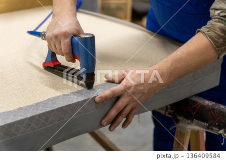 Worker's hand operates a blue pneumatic stapler. Worker's hand operates a blue pneumatic stapler. 136409584
