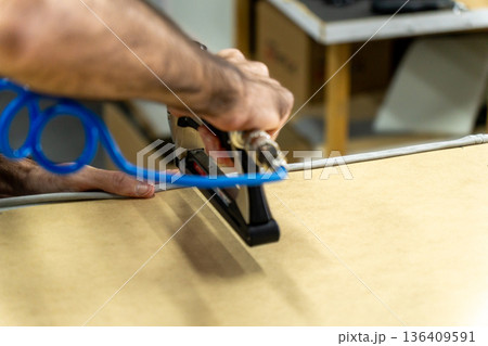 Close-up of upholsterer using a pneumatic staple gun to attach fabric to a wooden furniture frame. 136409591