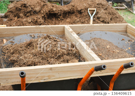 Close up of sieve with rich organic soil and compost on wheelbarrows. 136409615