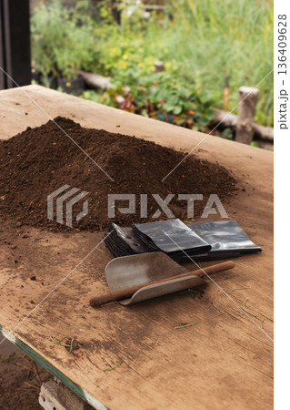 Vertical real picture of rich soil and organic compost mix on a wooden surface with a small shovel for planting trees 136409628
