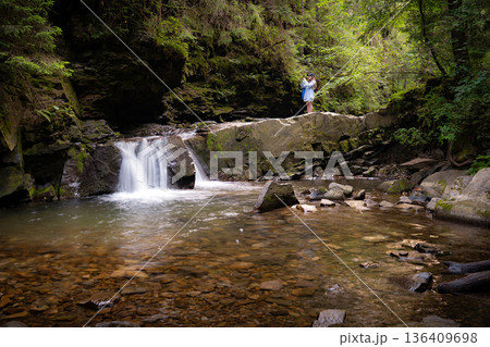 Woman Taking Photos on Stone Ledge Above Forest Waterfall Woman Taking Photos on Stone Ledge Above Forest Waterfall 136409698