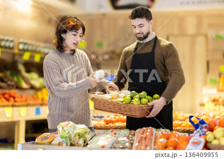 Girl customer in vegetable store examines radish, male seller advises and help with choice 136409955