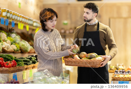 Male salesperson offers a female customer mango for sale 136409956