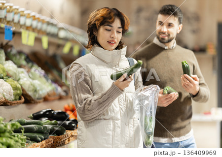 Couple near vegetable stand in store choose zucchini. 136409969