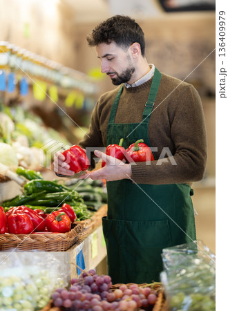 Man seller in grocery vegetable shop arrange bell pepper case Man seller in grocery vegetable shop arrange bell pepper case 136409979