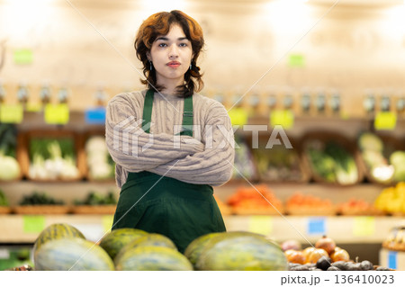 Portrait of young female grocery store employee in fruit and vegetable department Portrait of young female grocery store employee in fruit and vegetable department 136410023