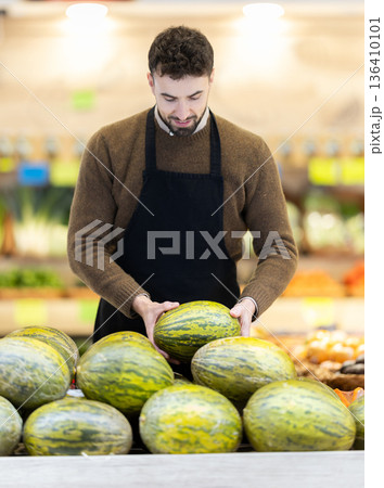 Young man seller puts melon in store Young man seller puts melon in store 136410101