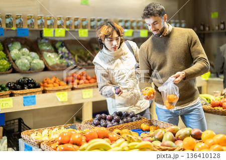 Couple shopping in vegetable store and buy elect fruits plum and persimmon. Couple shopping in vegetable store and buy elect fruits plum and persimmon. 136410128