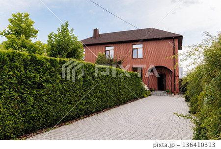 Brick house with long driveway and tall evergreen hedge, suburban residential exterior Brick house with long driveway and tall evergreen hedge, suburban residential exterior 136410313