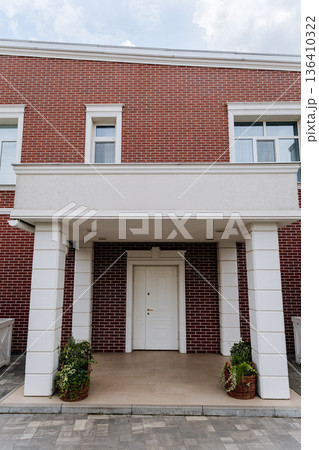 Front entrance of modern brick house with white columns, porch and closed door Front entrance of modern brick house with white columns, porch and closed door 136410322