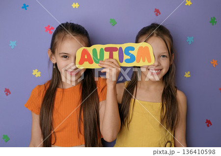 Two smiling children holding colorful autism sign with puzzle pieces. Autism awareness, social equality, neurodiversity support, inclusive education and childhood acceptance concept. 136410598