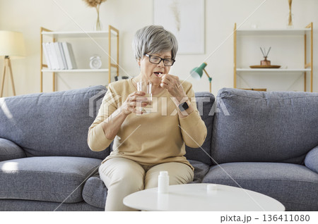 Senior woman taking pill dose at home, holding glass of water and capsule Senior woman taking pill dose at home, holding glass of water and capsule 136411080