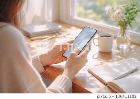 スマホと女性の手元 朝の日差しが差し込む窓辺のデスク スマホと女性の手元 朝の日差しが差し込む窓辺のデスク 136411102