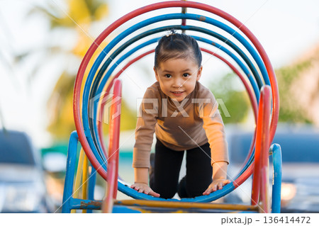 child girl crawling through a colorful metal tunnel structure at a playground 136414472