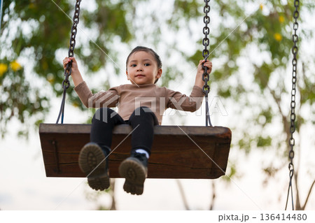 cheerful child girl playing on swing at playground 136414480