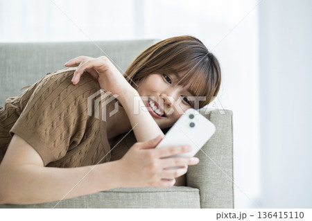 ソファーに横になってスマホを使う若い女性 ソファーに横になってスマホを使う若い女性 136415110