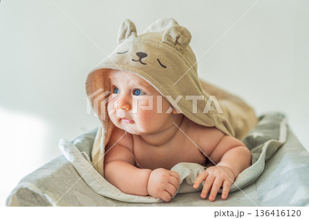 Baby lying on a changing table wrapped in a soft towel after bathing at home. Clean, calm and cozy moment of infant care and safety. Baby hygiene, daily routine and gentle parenting concept 136416120