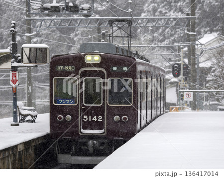 雪が積もる駅に入る能勢電鉄の電車 136417014
