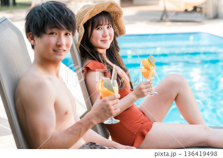 旅行,バカンスでプールサイドのサンラウンジャーに座る水着姿の男女カップル 旅行,バカンスでプールサイドのサンラウンジャーに座る水着姿の男女カップル 136419498