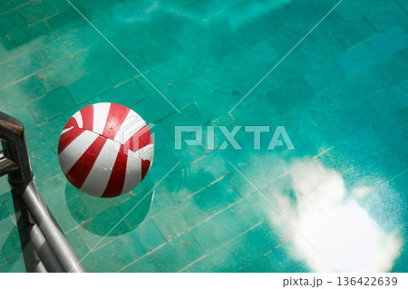 A beach ball floats on clear water near a poolside A beach ball floats on clear water near a poolside 136422639