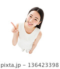 指を立てて上を指差すハイアングルの白い服の若い女性（俯瞰・切り抜き・コピースペース・白バック） 136423398