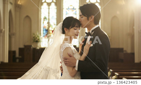 ステンドグラスを背景に新婦のおでこに優しくキスをする日本人新郎 136423405