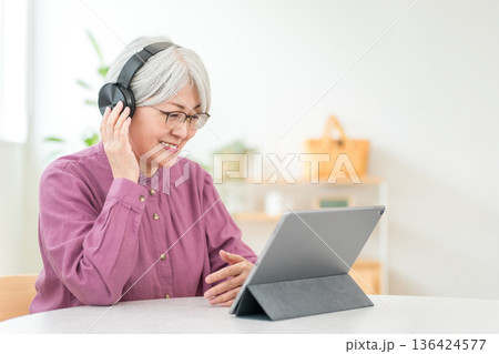 タブレットを見ながらヘッドフォンで音楽を聴くグレイヘアのアジア人女性 タブレットを見ながらヘッドフォンで音楽を聴くグレイヘアのアジア人女性 136424577