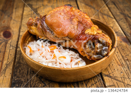 Crispy roasted pork knuckle shank with golden crackling rind served with fermented cabbage slaw on rustic wooden background. Crispy roasted pork knuckle shank with golden crackling rind served with fermented cabbage slaw on rustic wooden background. 136424784