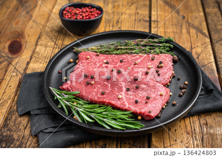 Fresh uncooked wagyu beef top round with rich marbling cooked style setup. Cast iron pan on rustic wood background. Fresh uncooked wagyu beef top round with rich marbling cooked style setup. Cast iron pan on rustic wood background. 136424803