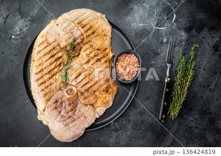 Juicy grilled pork shoulder whole cut with bone on black plate dark background food styling with fresh thyme and spices Juicy grilled pork shoulder whole cut with bone on black plate dark background food styling with fresh thyme and spices 136424819