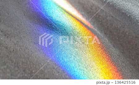 グレーの布地に差し込む鮮やかな虹色のプリズム光、質感が美しいファブリックテクスチャの抽象背景素材 136425516