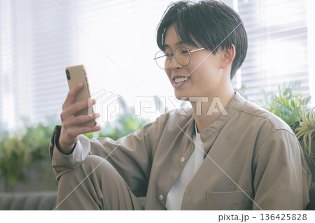 部屋でスマホを見る男性 136425828