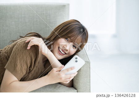 若い女性 スマホ 笑顔 カメラ目線 ソファー 若い女性 スマホ 笑顔 カメラ目線 ソファー 136426128