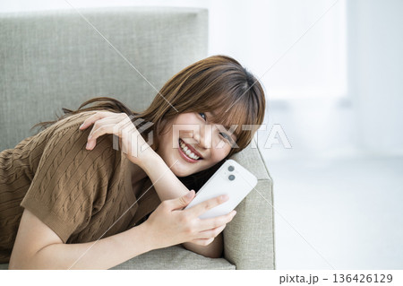 若い女性　スマホ　笑顔　カメラ目線　ソファー 136426129