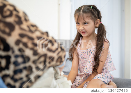Asian kid daughter grinning to a mother organizing school bag while sitting on sofa in living room. Asian kid daughter grinning to a mother organizing school bag while sitting on sofa in living room. 136427456
