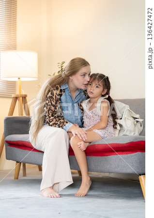 Caucasian whites mother talking or whispering to kid daughter while sitting on sofa in a living room Caucasian whites mother talking or whispering to kid daughter while sitting on sofa in a living room 136427472