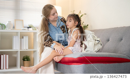 Caucasian whites mother talking to asian girl kid daughter with school bag on sofa in a living room. Caucasian whites mother talking to asian girl kid daughter with school bag on sofa in a living room. 136427473
