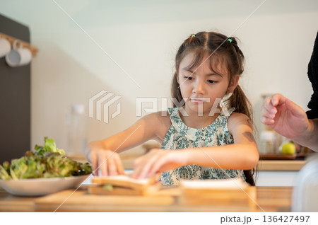 Asian kid daughter putting breads together making a sandwich with mother at kitchen cooking counter. 136427497