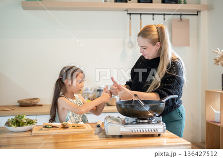 Asian daughter and white mother giving thumb up to each other standing at cooking counter in kitchen Asian daughter and white mother giving thumb up to each other standing at cooking counter in kitchen 136427512