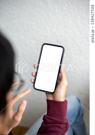 A man holding white screen smartphone looking or reading while sitting beside white wall in a cafe. 136427588
