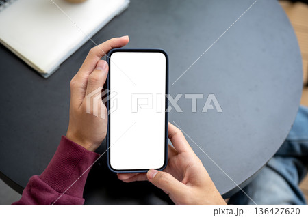 A man hand holding white screen smartphone reading or looking while sitting at black table in a cafe 136427620