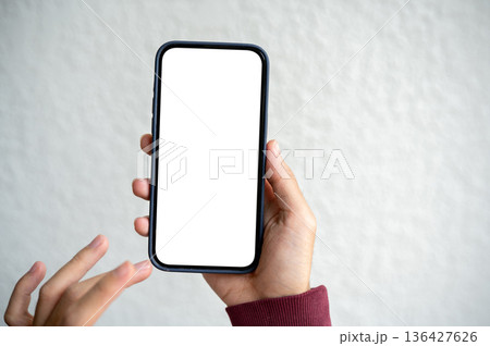 A man's hand holding blank screen smartphone with finger pointing beside white wall in a cafe. A man's hand holding blank screen smartphone with finger pointing beside white wall in a cafe. 136427626