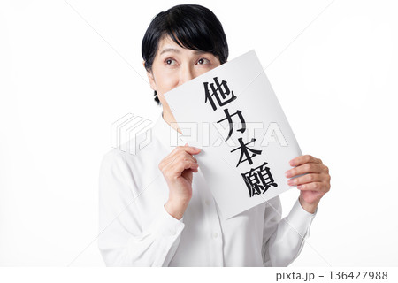 他力本願と書かれた紙を持ち何かたくらんだ表情のシニア女性 他力本願と書かれた紙を持ち何かたくらんだ表情のシニア女性 136427988