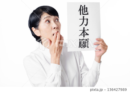 他力本願と書かれた紙を持ち口元を手で押さえる白いシャツを着たシニア女性 136427989