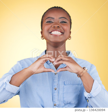 Black woman, heart hands and health with emoji, smile in portrait and love isolated on yellow background. Support, care and kindness with respect, happiness and wellness, romance sign in a studio 136428094